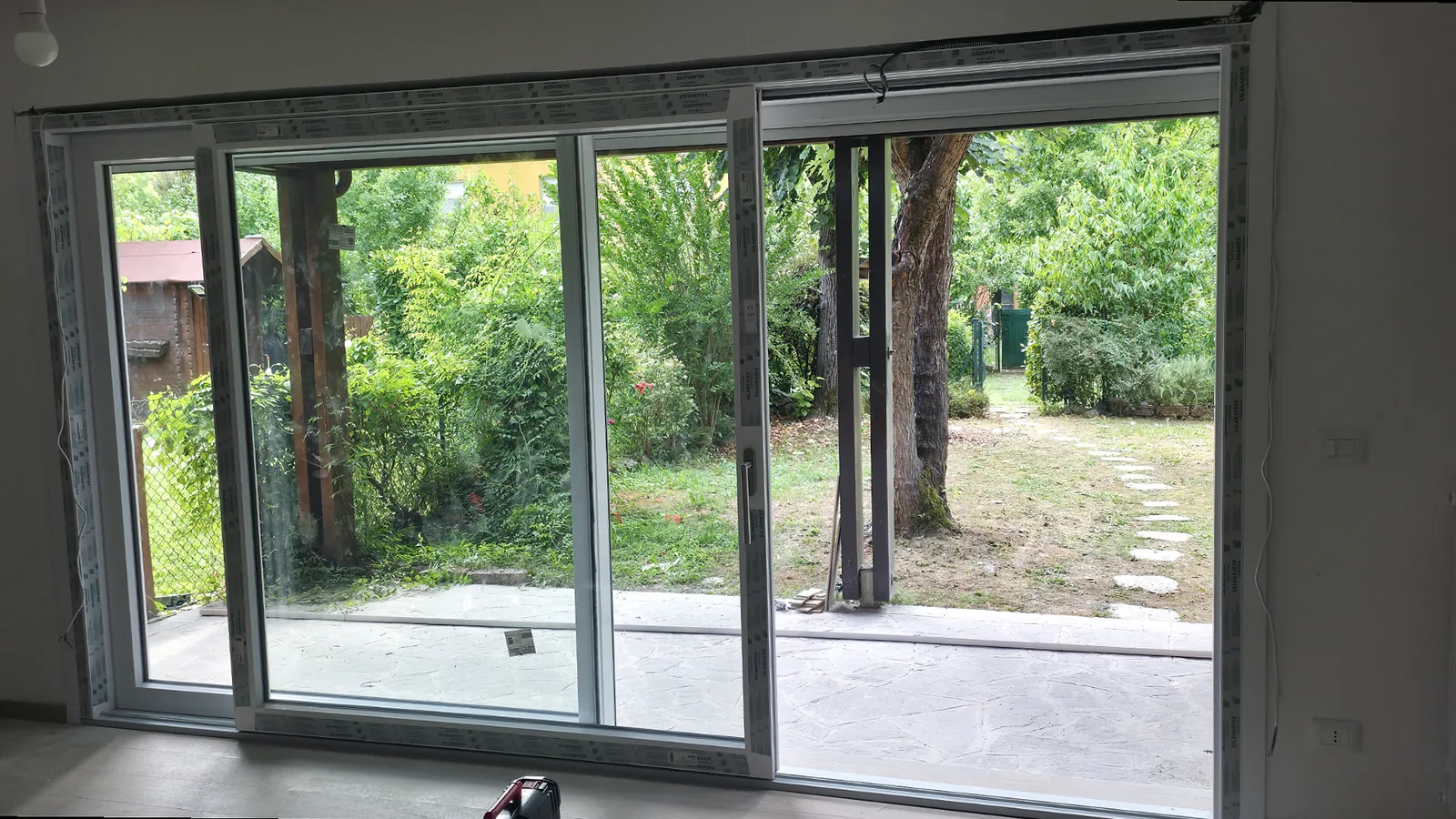 Portafinestra scorrevole con telaio scuro, vista dall’interno sul giardino